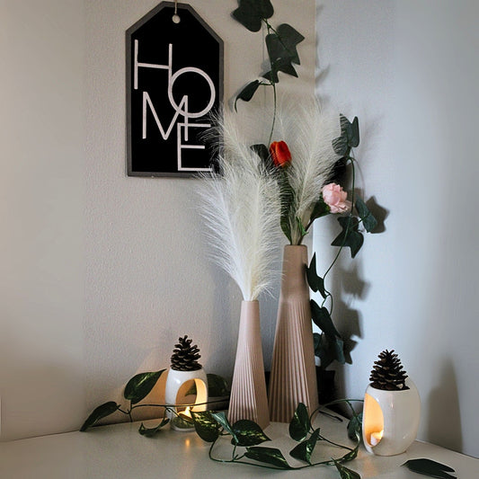Decorative setup with vases, candles, and plants on a table against a white wall with 'HOME' sign.