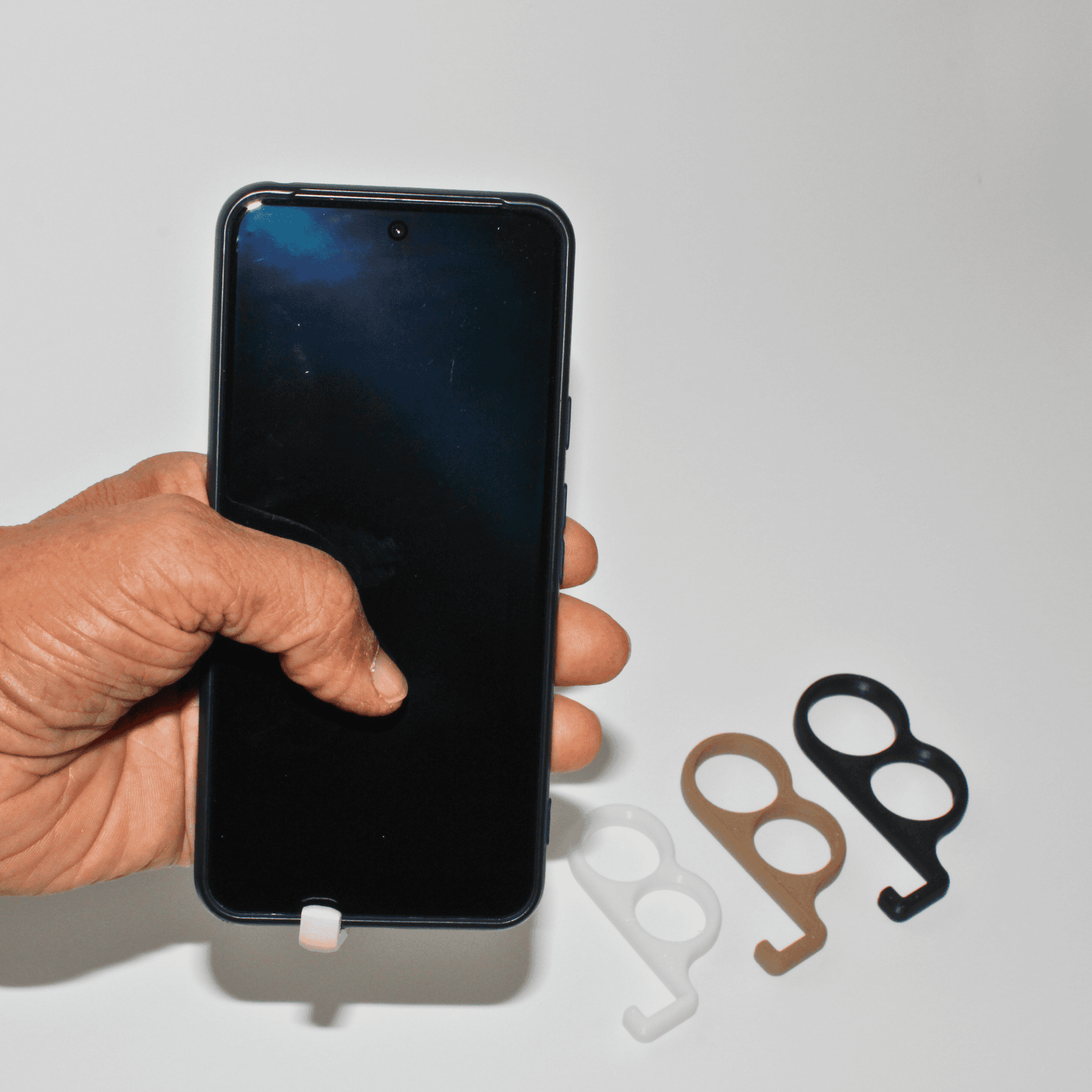 Hand holding a smartphone with two metal phone stands on a light gray background